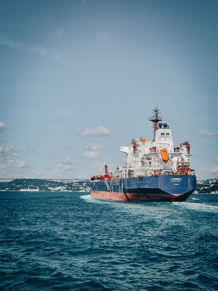 A cargo ship sails on a vast ocean under a clear sky, showcasing maritime transport.